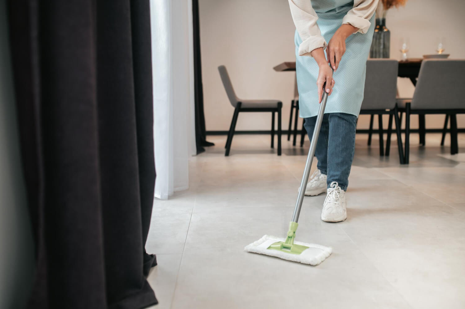 cropped female cleaner wipes living room floor with broom