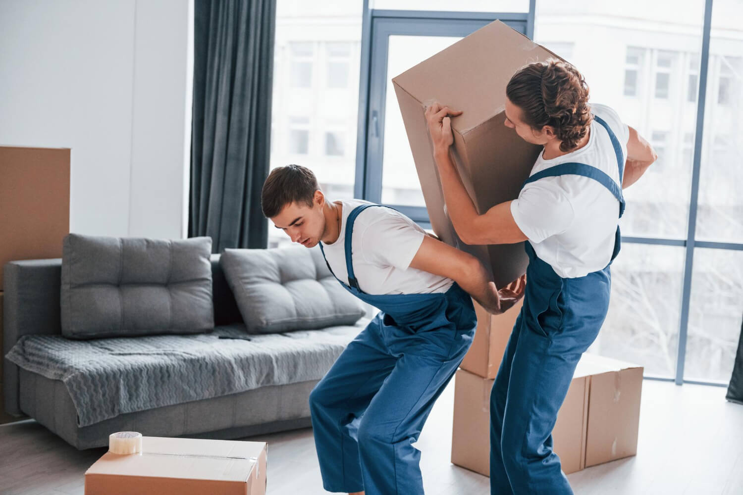 two movers in blue uniform try to carry heavy moving boxes for relocation