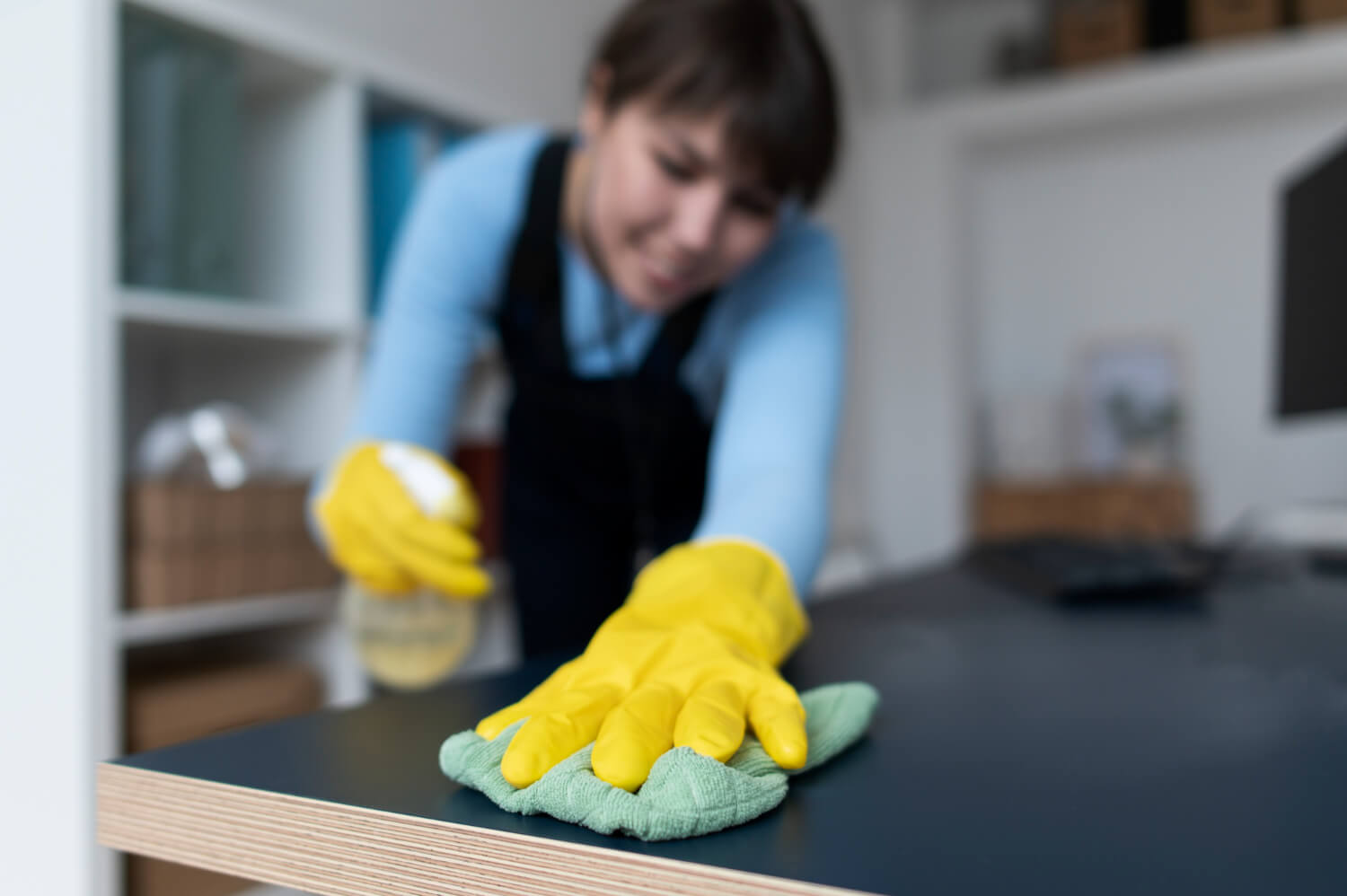 close up blurred cleaner in yellow gloves cleaning table with spray and green cloth focus