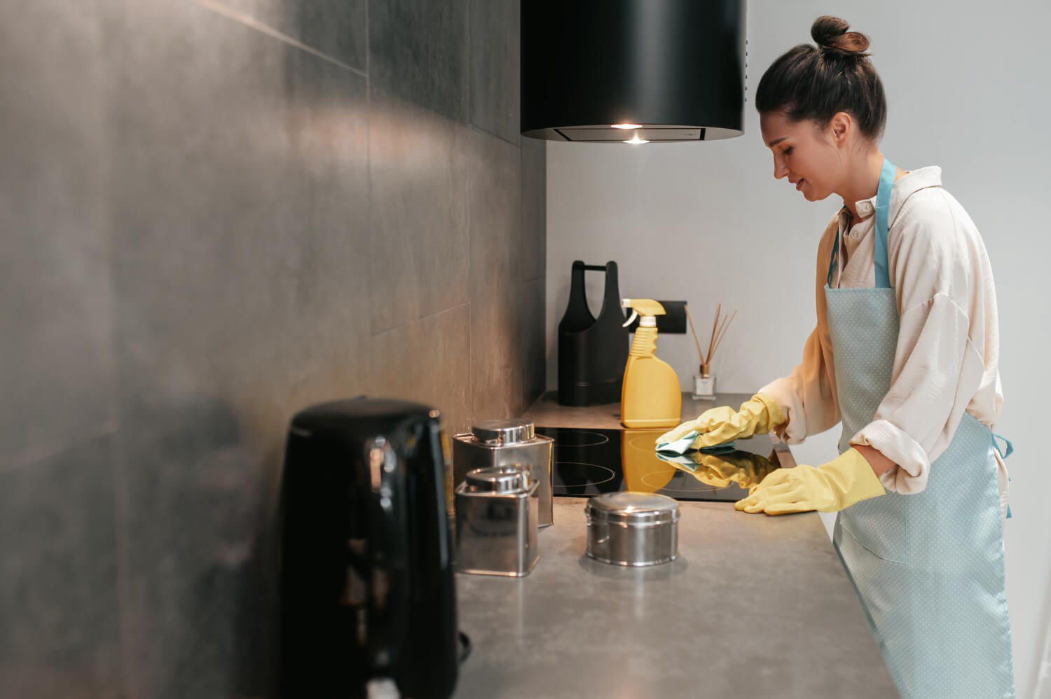 young dark haired woman in yellow protective gloves disinfecting kitchen surfase side view
