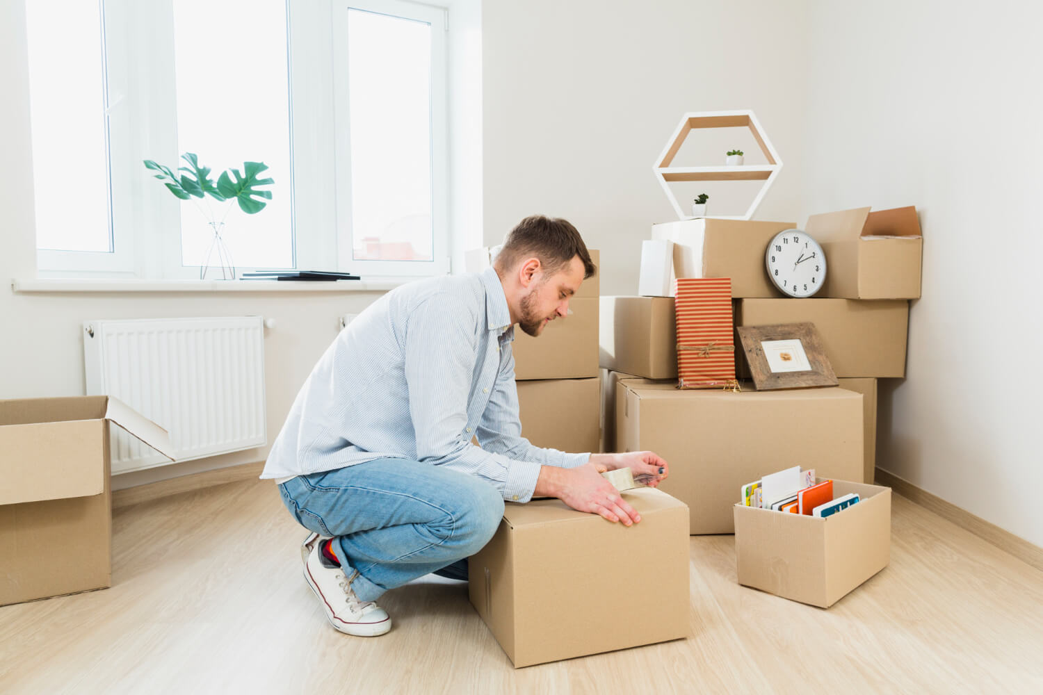 young man packing the cardboard boxes at his home with other boxes and belongings for relocation around him