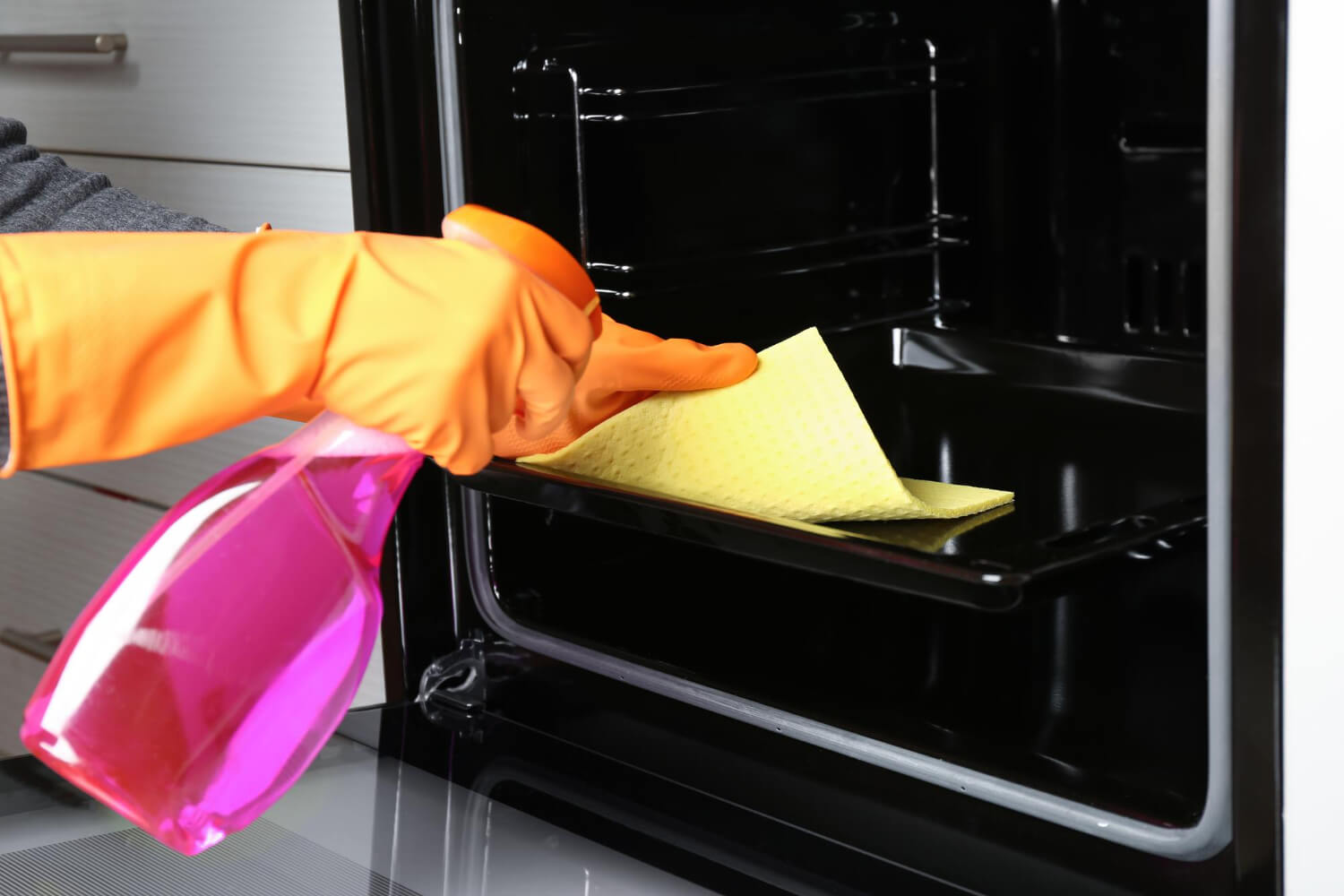woman with orange gloves cleaning inside of the oven with pink bottle spray