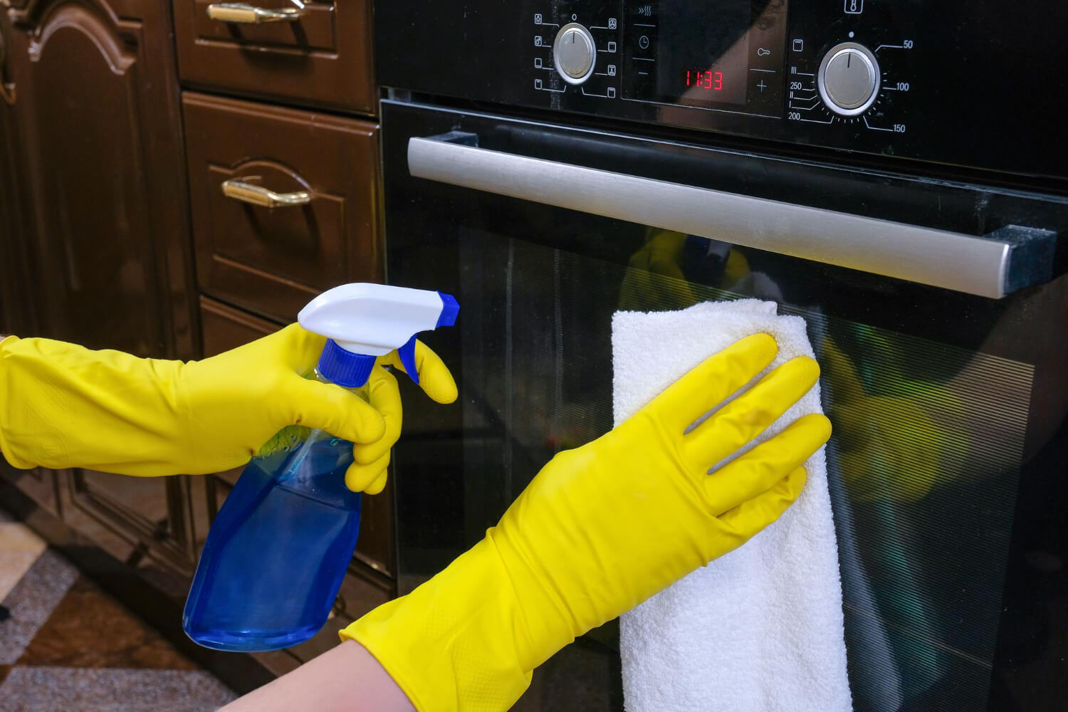 hands with rubber gloves clean oven with rag detergent wipe