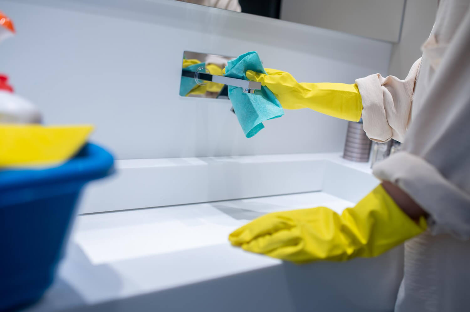 close up cropped female cleaner in the bathroom cleaning sink with blue cloth while wearing yellow gloves