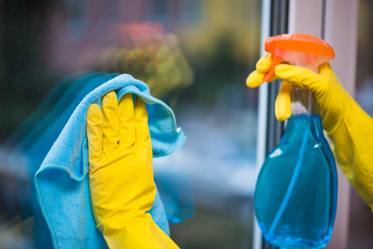 close up cleaners hands in yellow gloves cleaning window with spray and blue cloth