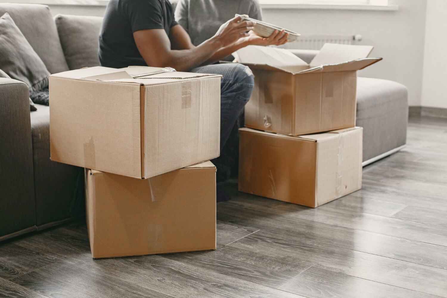 two homeoners siting on sofa in empty living room and putting things in moving boxes