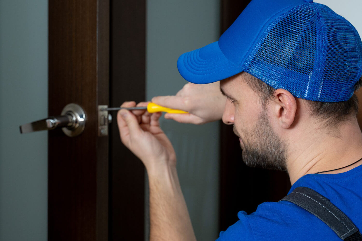 handyman with blue uniform and blue hat repairing door lock close up