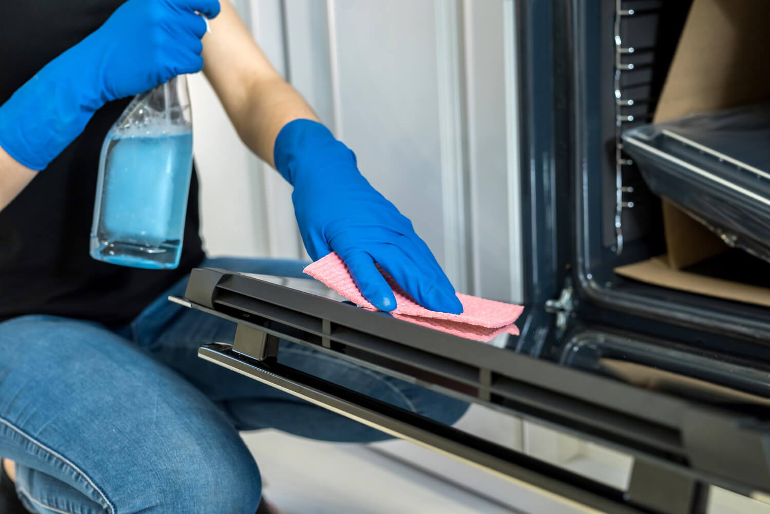 young woman cleaning oven with blue rubber gloves close up