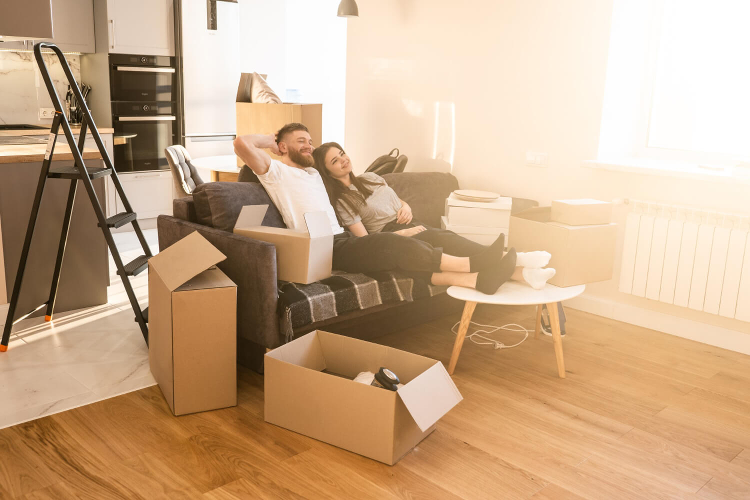 happy couple resting on sofa at their new home with staffed moving boxes around them