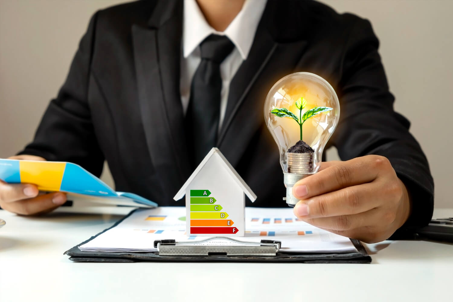 businessman hand holding energy saving light bulb with plants growing coins light bulbs on desk