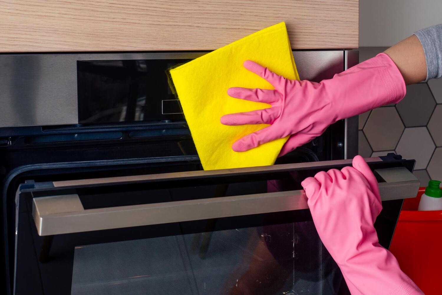 young crop woman with pink gloves cleaning oven kitchen at home