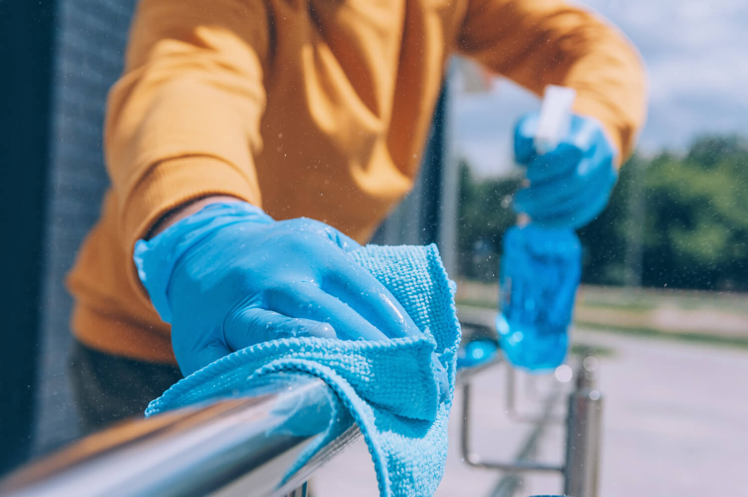 close up young cleaners hand cleaning railing with blue gloves and blue rug