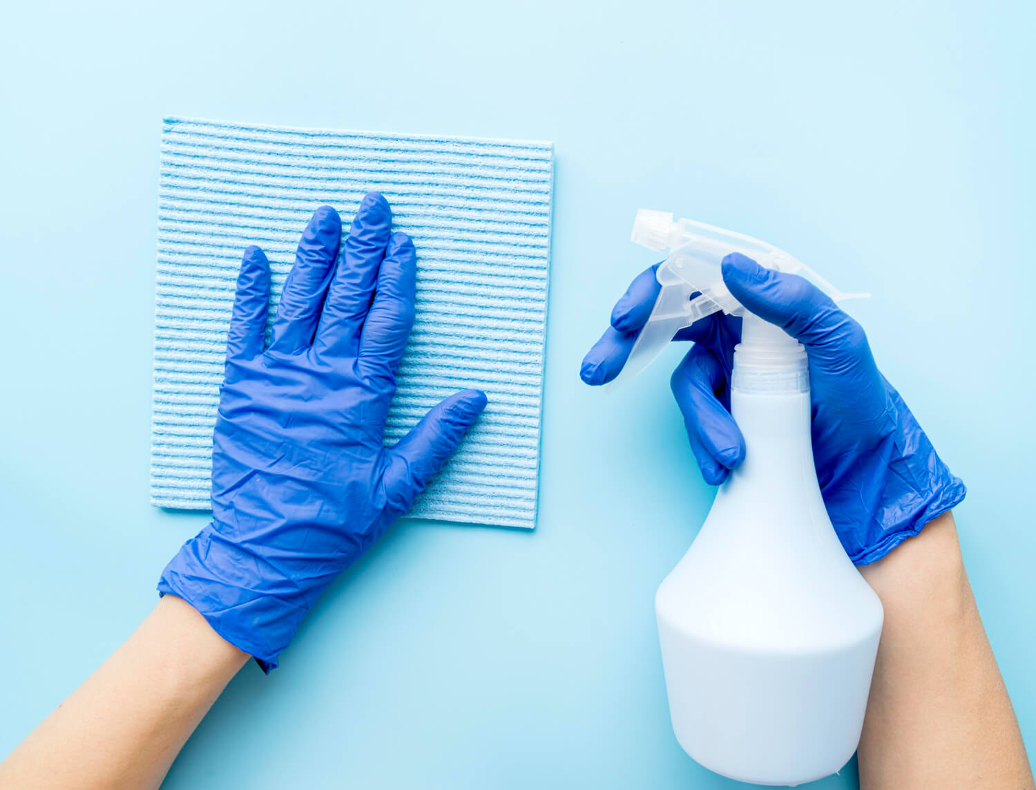 close up female hands in blue protective gloves holding cleaning spray and blue cloth in blue backround