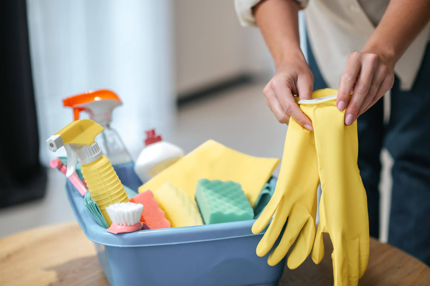 close up female hands holding yellow gloves and a blue backet of cleaning equipment