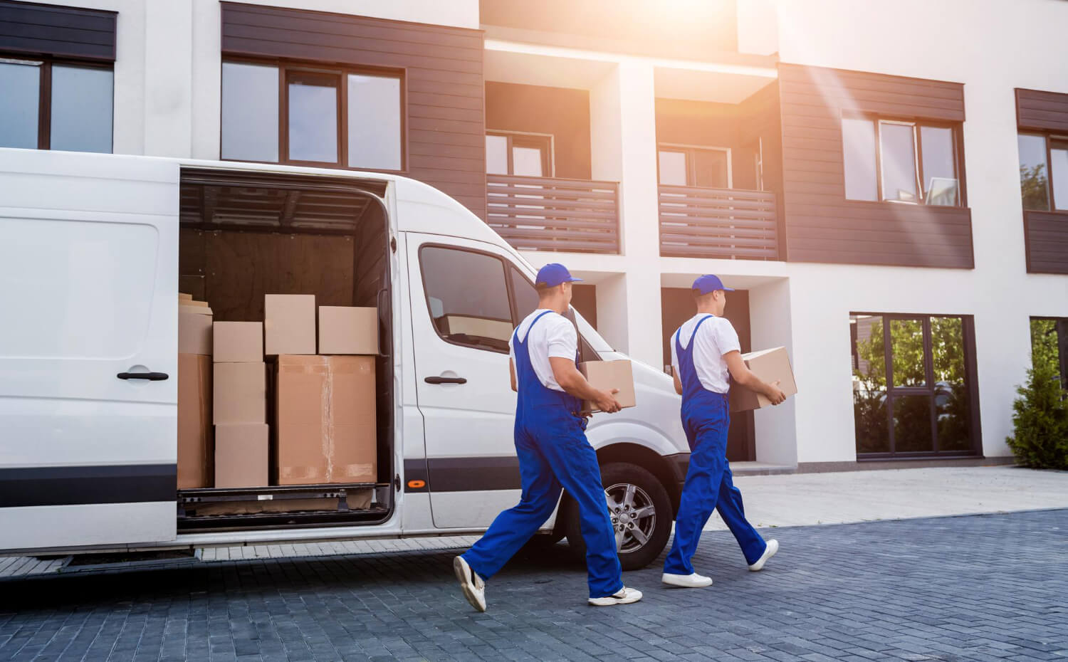 two movers unloading boxes from a white van to new home