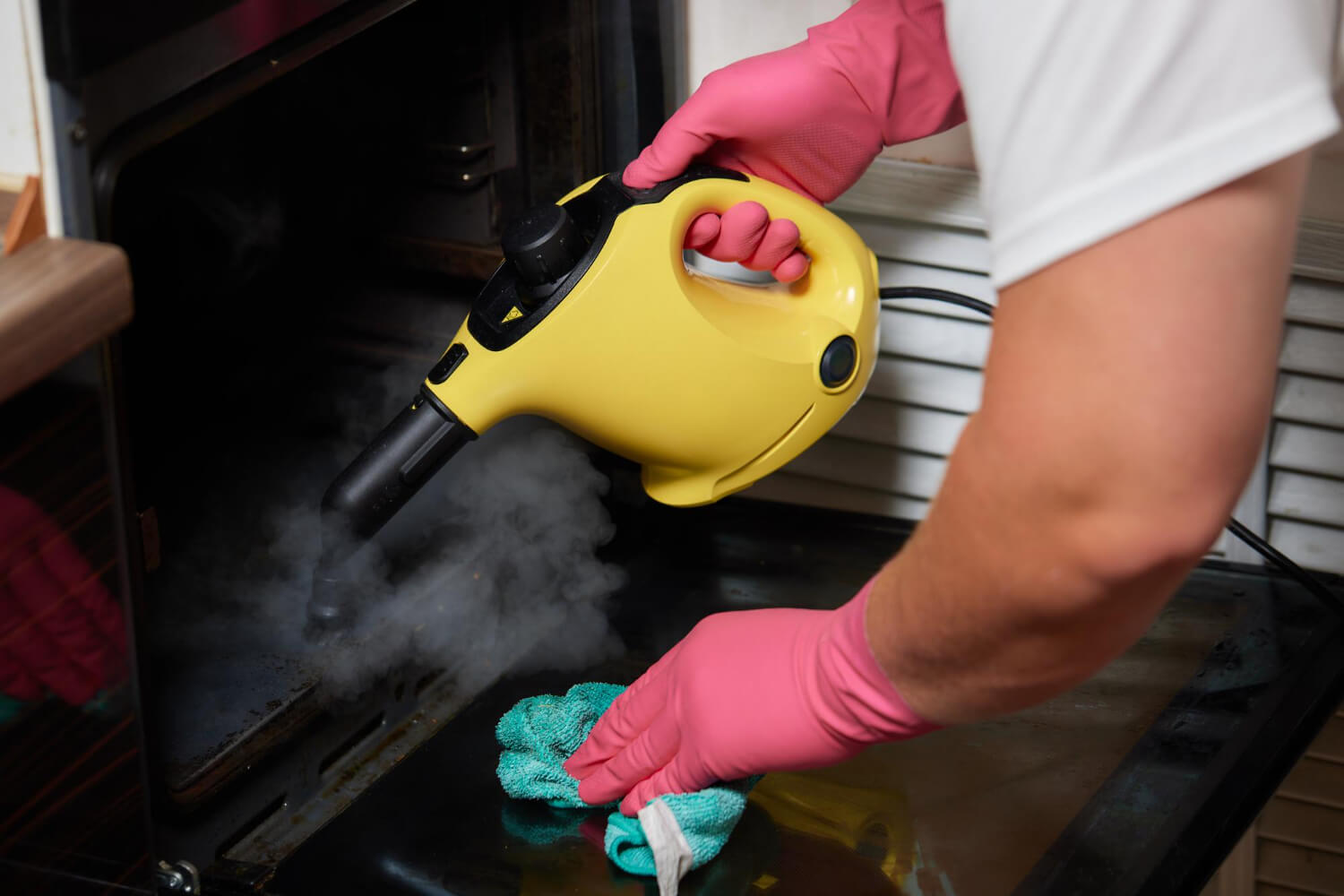 experienced cleaner with rubber gloves stemcleaning the inside of the oven