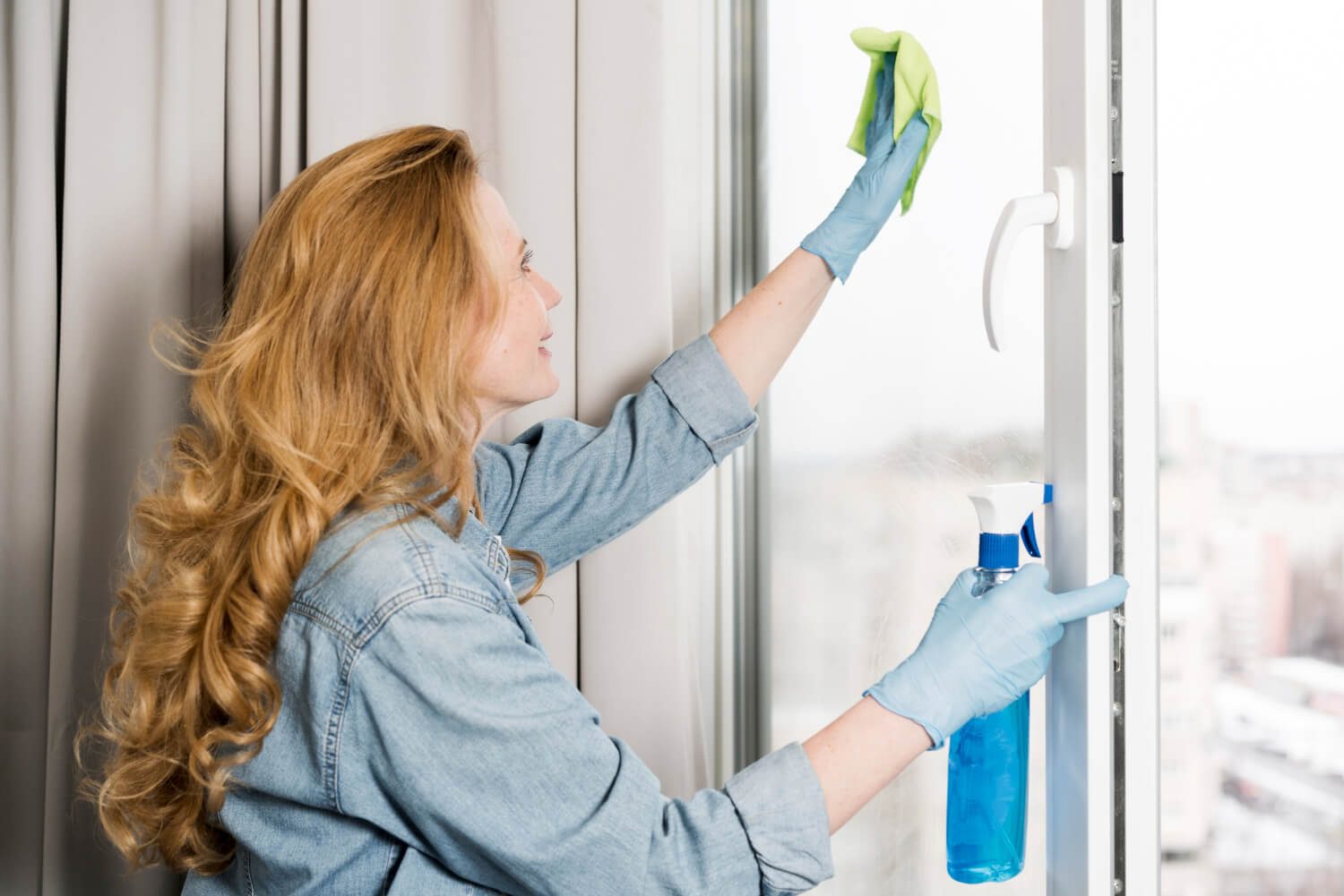 side view of woman wiping window with spray and cloth